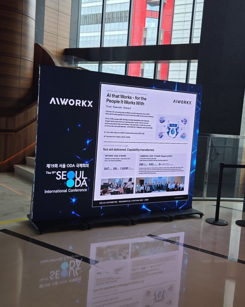 AIWORKX 부스 벽면 그래픽. 헤드카피 ‘AI that Works — for the People It Works With’와 ‘Not aid delivered. Capability transferred.’, KOICA IBS 베트남과 캄보디아 사업 소개